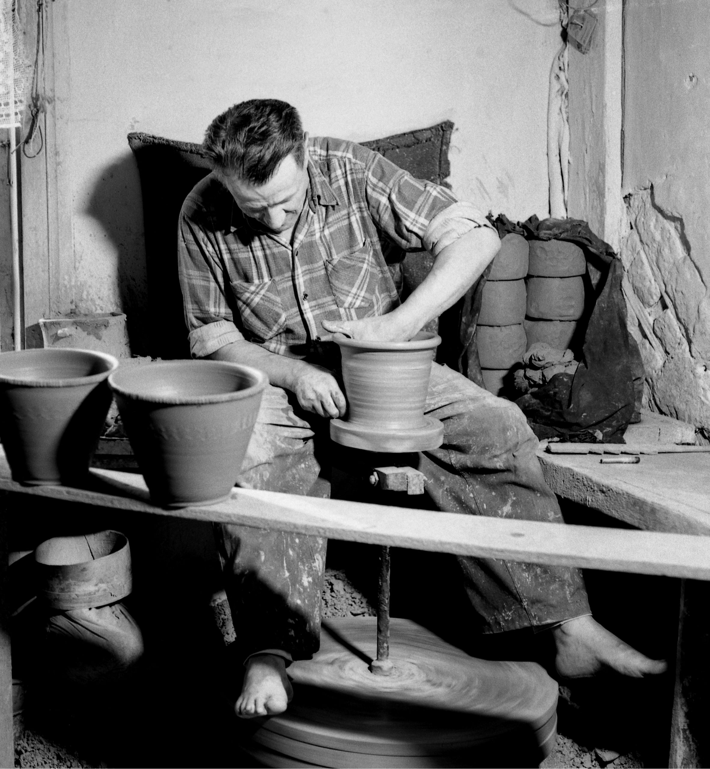 Czarno białe zdjęcia z 1974 roku przedstawia garncarza z Siemiatycz podczas pracy na kole. Przed garncarzem stoją dwa wykonane już gliniane obiekty, najpewniej donice.
