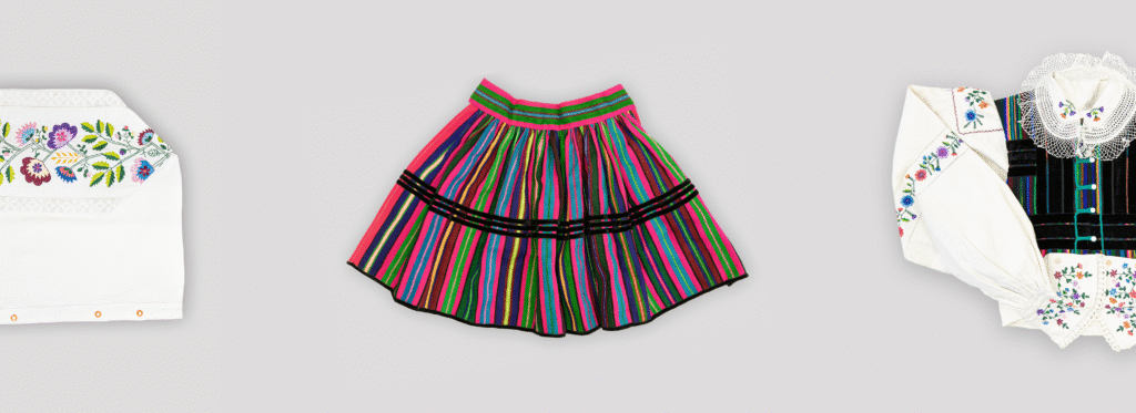 Biała bluzka z kolorowym kwiatowym haftem, spódnica w paski w kolorach zielonym, różowym, niebieskim i czarnym oraz biała bluzka z koronkowym kołnierzykiem i kwiatowym haftem obok czarnej kamizelki; wszystko na jasnoszarym tle.